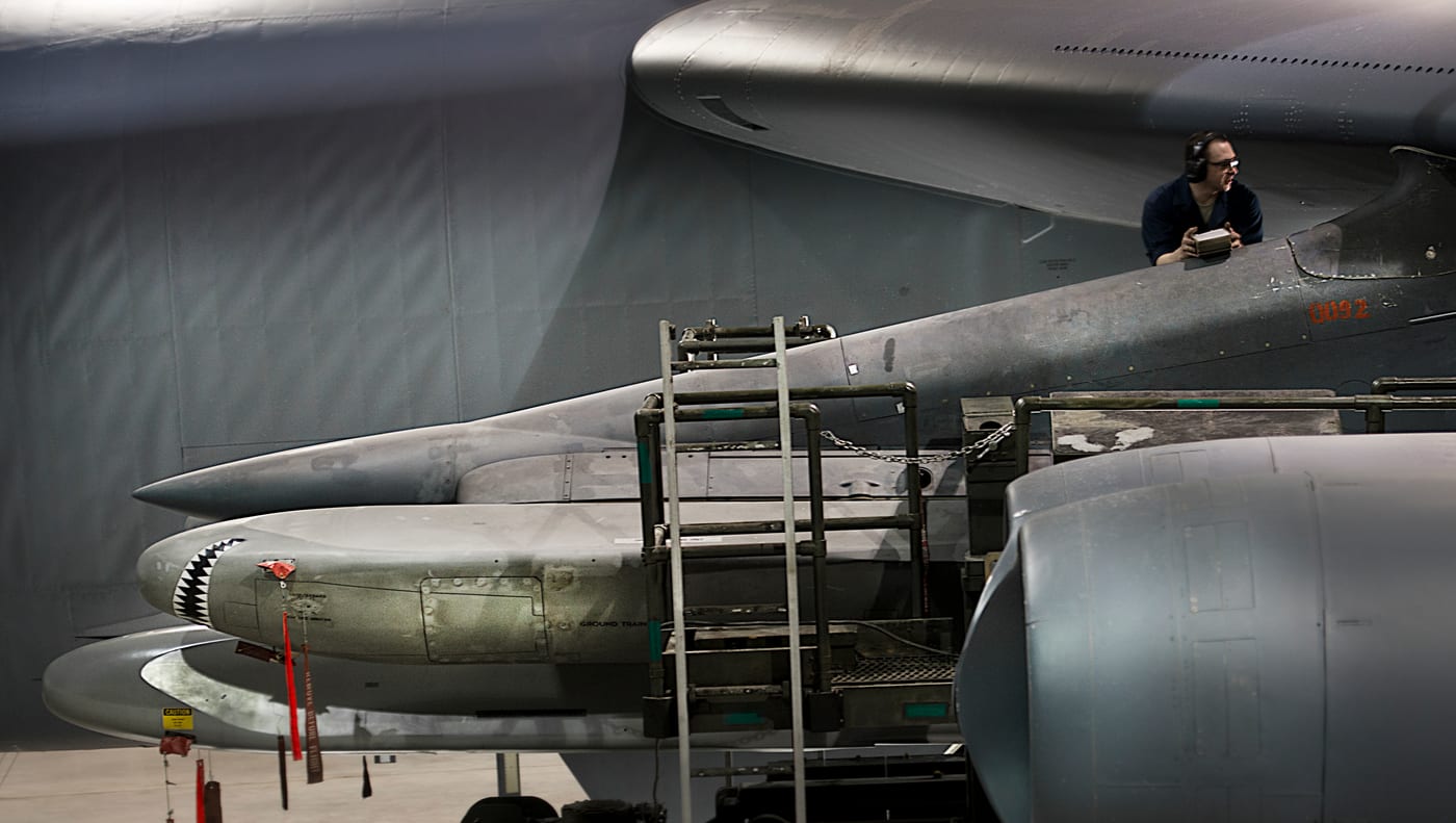 AGM-86 cruise missiles mounted on an underwing pylon of a B-52 Stratofortress, with a maintainer working above them