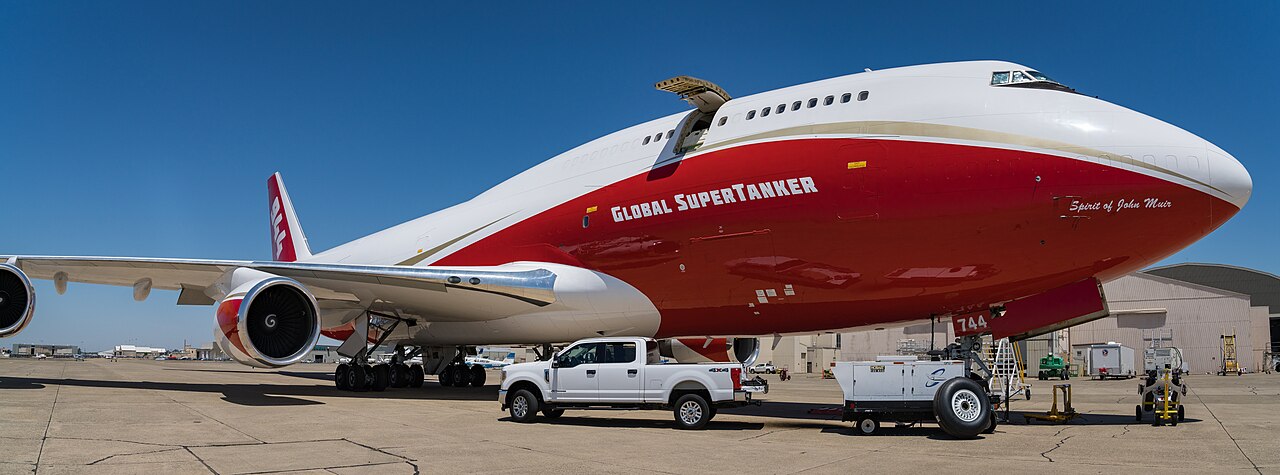 The white-and-red Global SuperTanker Boeing 747 flying low across open terrain while releasing a long line of red fire retardant